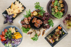 Grilled meats presentation | Top view of an assortment of grilled meats, Georgian cuisine snacks, cheese, and vegetable cuts on a white wooden table. | Bar-B-Clean